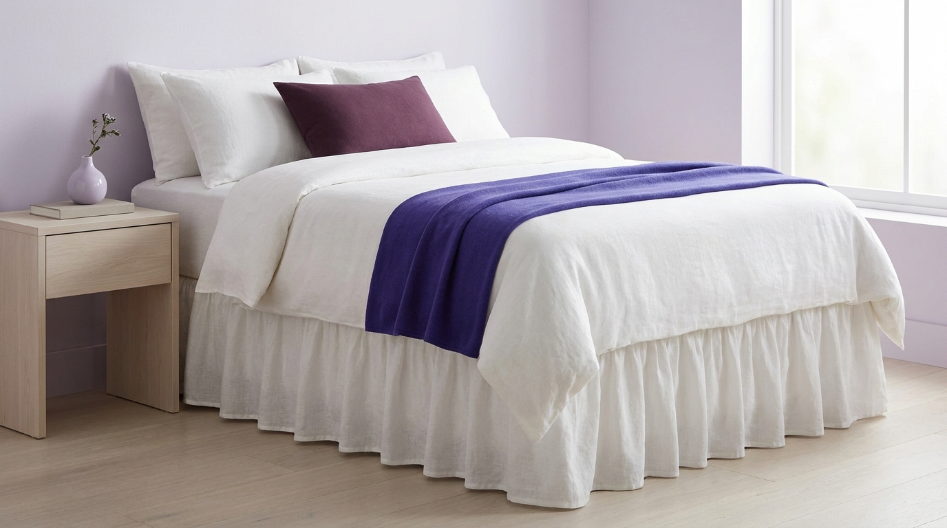Minimalist bedroom with neatly made bed and visible bed skirt under soft natural light neutral linens and subtle brand color accents